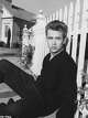 James Dean sits on the ground, leaning on a picket fence in a publicity still for “East of Eden” (1955).