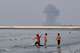 Three boys play in the shallow waters of the Strait of Hormuz, as a plume of smoke rises from an explosion in the background, off Bandar Abbas, Iran, Monday, July 13, 2026. (Razieh Poudat/ISNA via AP)
