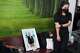 A relative of a musician Preutthipong Pudmon victim, a victim in a music bar fire, stands beside his portrait as she receives his body at a police hospital in Bangkok, Thailand, Wednesday, July 15, 2026.
