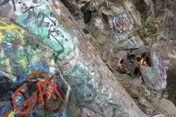 People warm themselves by a fire near graffiti-covered rocks near Sapphire Falls in Cucamonga Canyon on June 23, 2013, in the Angeles National Forest near Rancho Cucamonga, Calif.