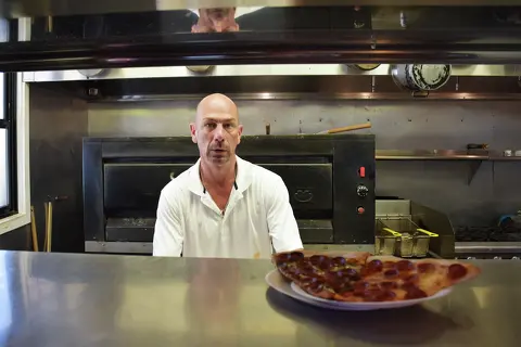 David Rosner, owner of Rozzi Pizza in Santa Barbara, Calif., takes a look over the counter after serving up a couple of signature slices on July 30, 2026.