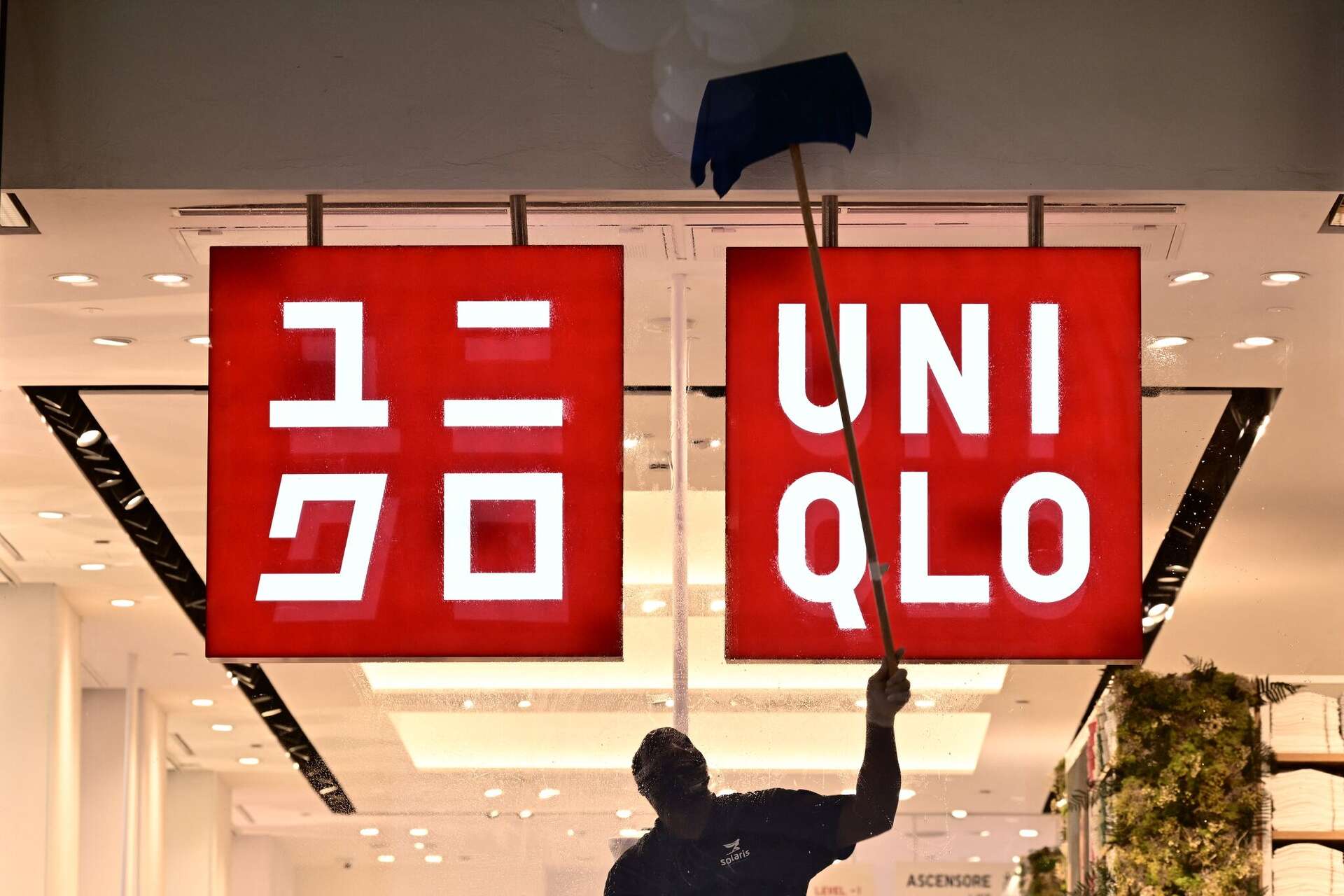 A worker cleans around a Uniqlo sign in a store in 2024. Uniqlo is reopening in downtown San Francisco Friday, Oct. 9, with a new flagship store and a free stre