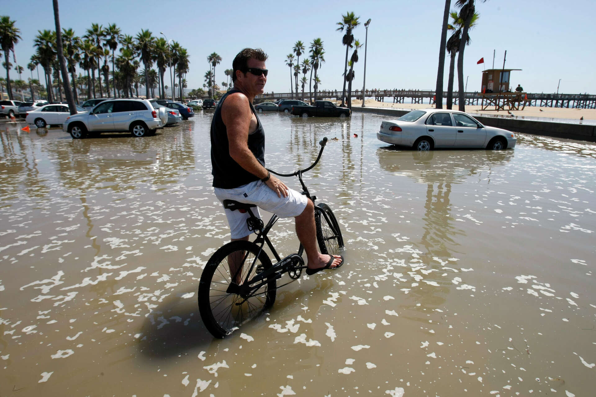 A Newport Beach, Calif., man sits on his bike at the flooded Balboa Peninsula pier parking lot during a previous high tide event in 2011.