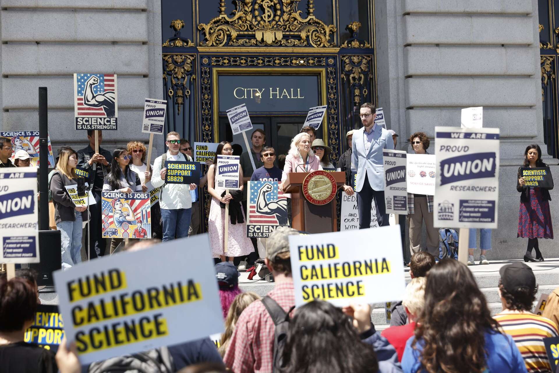 Scientists from UCSF, UC Berkeley and Stanford, community members and state Sen. Scott Wiener rally in San Francisco on May 16, 2025 to support a ballot measure