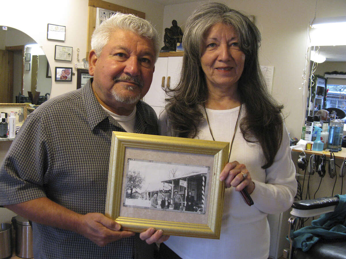 Siblings Louie and Paulette Sanchez show off a photo that reflects the Sanchez Barber Shop in its early years. The firm on Main Street in Kerrville just celebrated its first century in business.