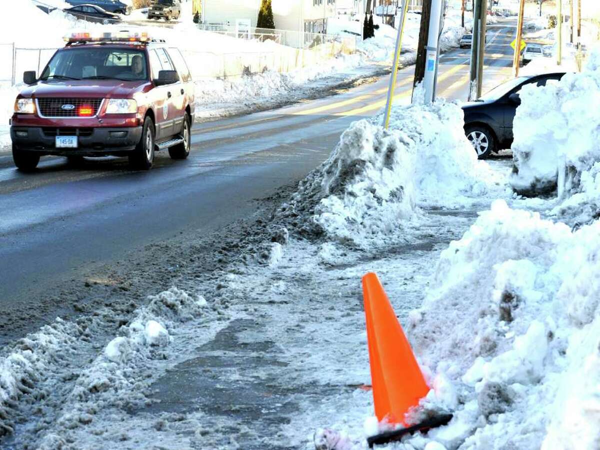 A driver waits to pull onto New Street in Danbury, past piles of snow, as an emergency vehicle passes on Thursday, Jan. 13, 2011.