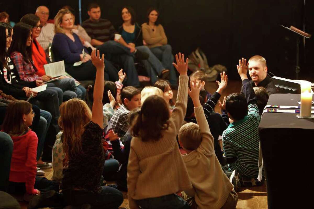 Pastor Adam West (right) sits down with children from the congregation during the church service Sunday at Braun Hall, a community dance hall and gathering place.  Photo by Marvin Pfeiffer