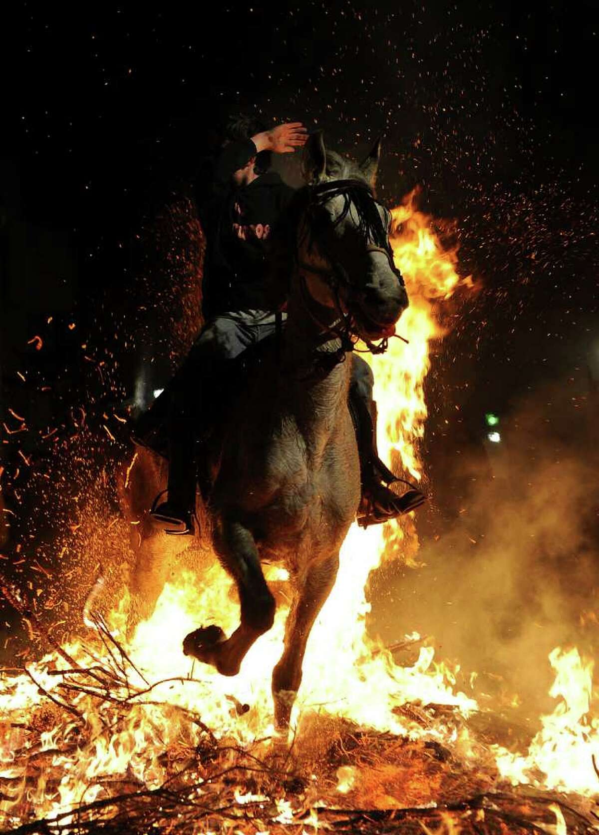 SAN BARTOLOME DE PINARES, SPAIN - JANUARY 16: A boy covers his face from the flames as he rides a horse through a bonfire on January 16, 2011 in the small village of San Bartolome de Pinares, Spain. In honor of San Anton, the patron saint of animals, horses are riden through the bonfires on the night before the official day of honoring animals in Spain. (Photo by Jasper Juinen/Getty Images)