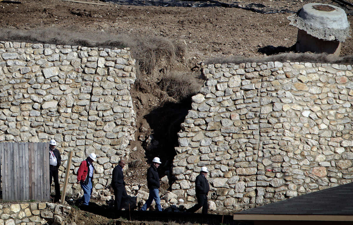 Men in hard hats walk past the fractured retaining wall in the RiverMist subdivision on the city's Northwest side on Friday, Jan. 29, 2010.