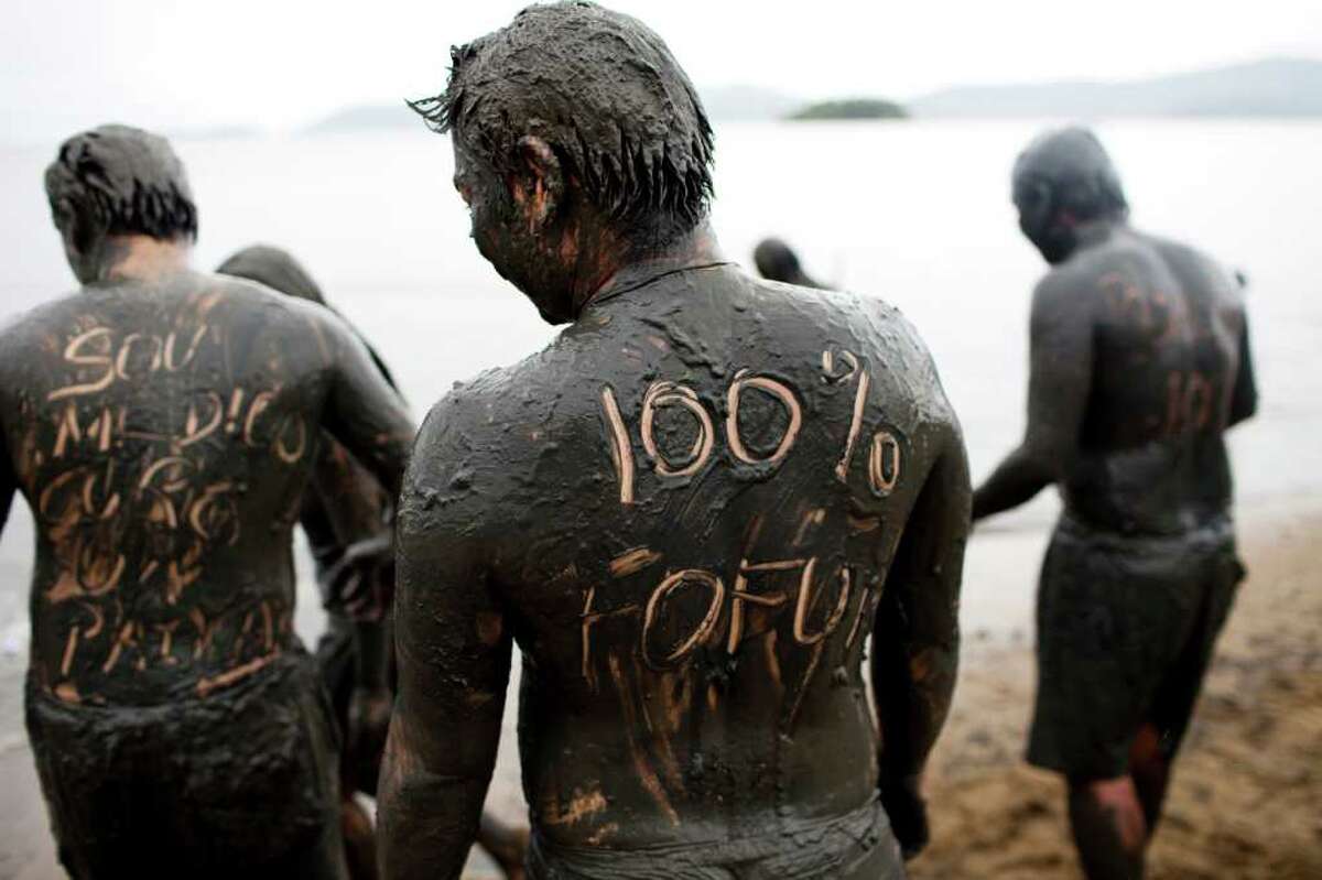 ** CORRECTS MEANING OF PORTUGUESE WORD FOFO TO HANDSOME ** Covered by mud, people participate in a mud party during Carnival celebrations in Paraty, Brazil, Saturday, March 5, 2011. The back of the man at center reads in Portuguese "100% handsome." (AP Photo/Rodrigo Abd)