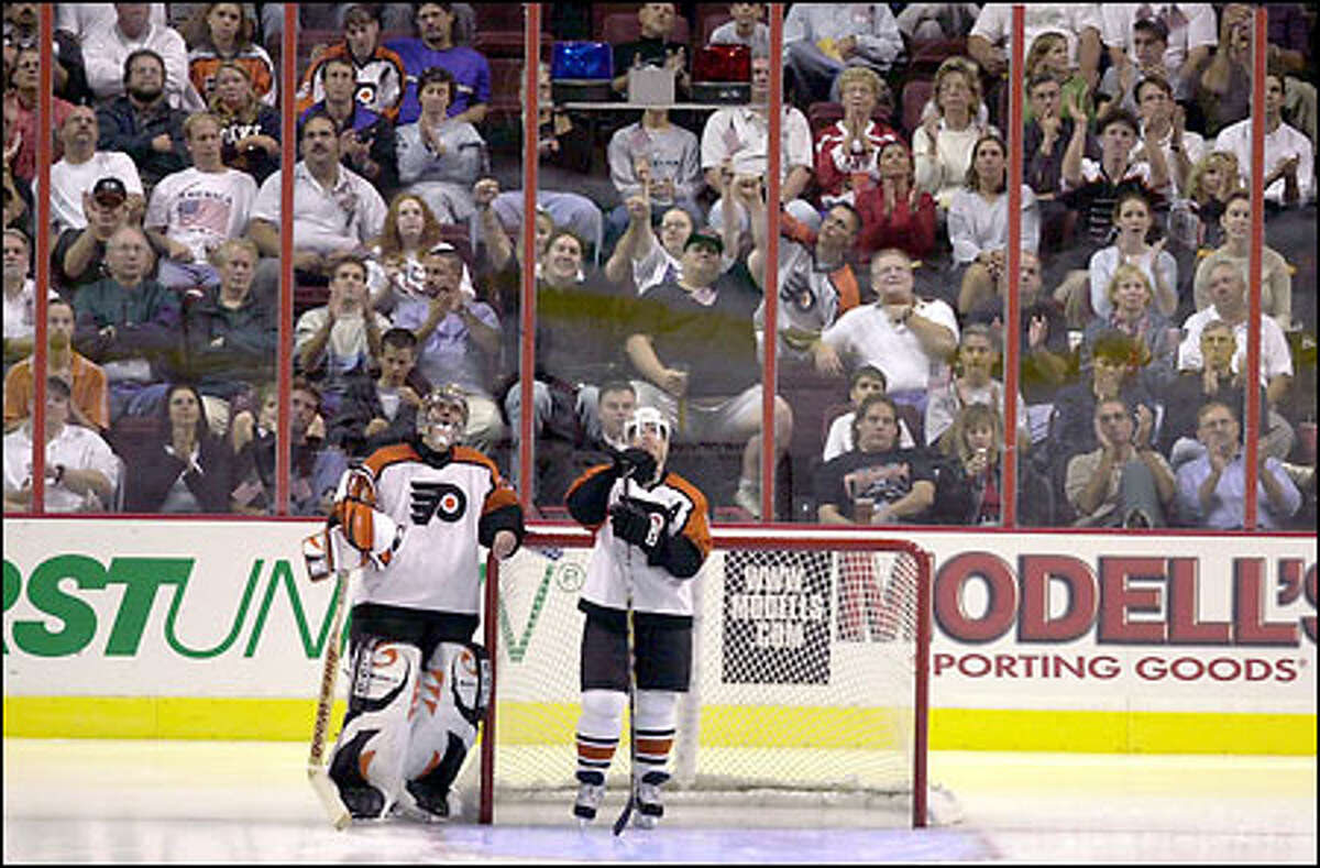Fans and two Flyers -- Brian Boucher, left, and Mark Recchi -- watch President Bush's nationally televised address in Philadelphia's First Union Center.