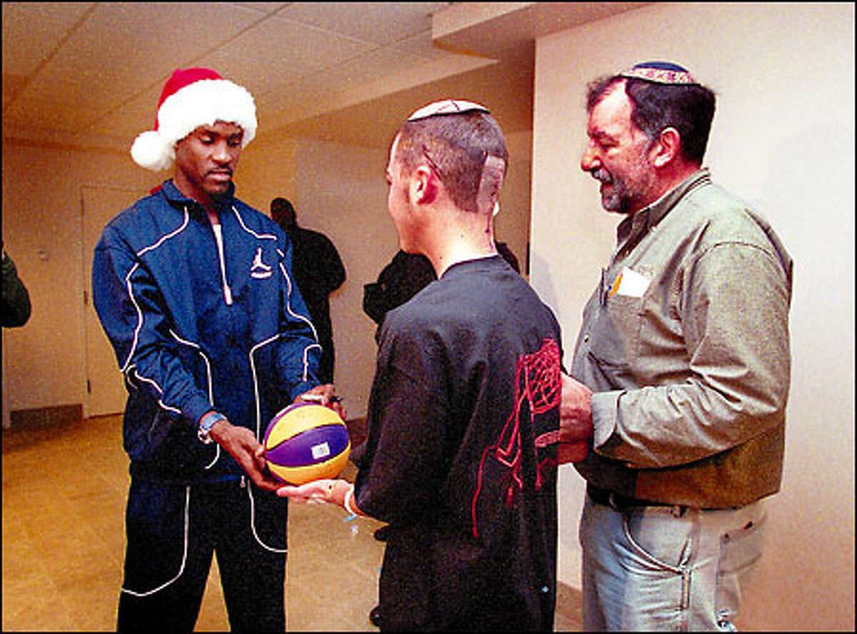 Sonics star Gary Payton autographs a basketball for Children's Hospital patient Ari Grashin, recovering from brain tumor surgery, as his father David Grashin looks on.