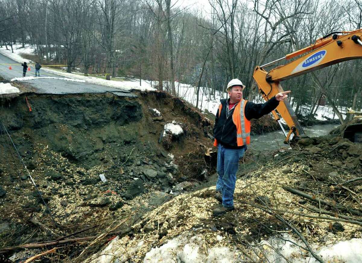 SPECTRUM/Matt Marshall of AT & T inspects the site of the collapsed roadway on Chinmoy Lane in New Milford Thursday. Work is underway to erect a 90-foot, temporary access bridge to Chinmoy. An access road to the back side of the street's cul de sac, through woods off West Meetinghouse Road, was well underway Friday.
