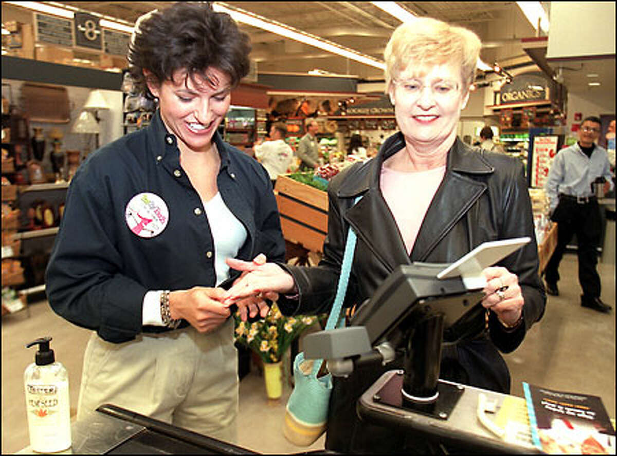 Margaret McGuire of Indivos Corp., left, helps Coleen Thompson use the new pay-by-touch system at West Seattle Thriftway yesterday.