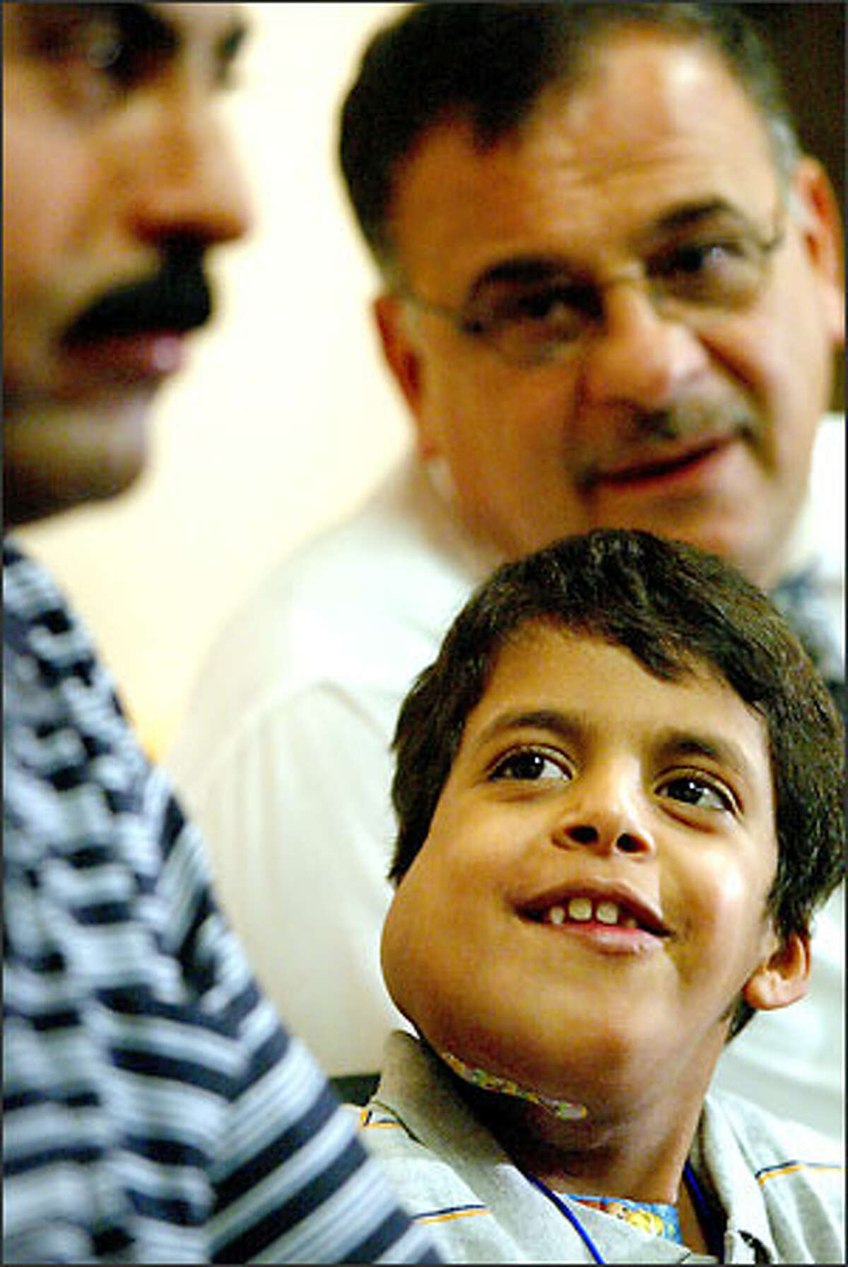 Ali Mousa Souad, 8, listens to Walid Farhoud's translation of a reporter's question for him and waits for his father, Mousa Souad, at left to answer for him.