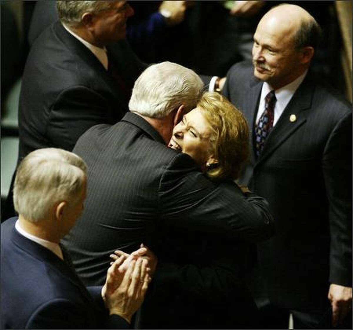 Christine Gregoire, flanked my husband Mike, right, is embraced by State Treasurer Mike Murphy after being sworn in as governor in the Legislative Building in Olympia.