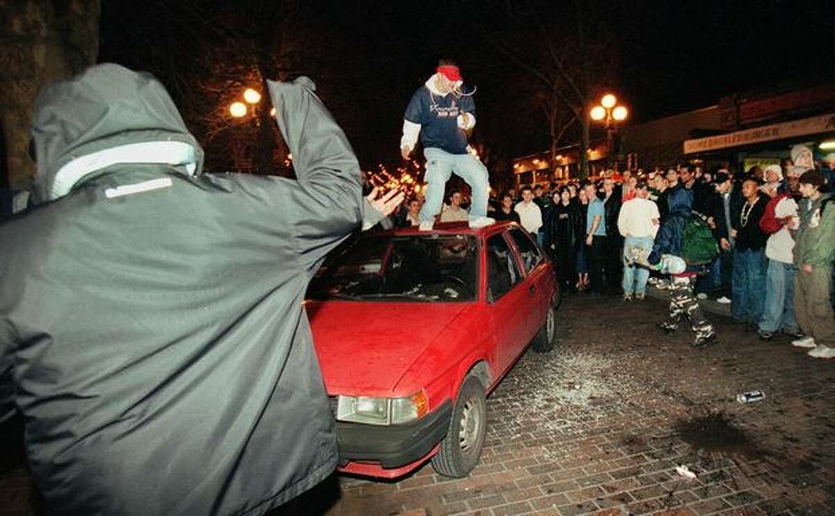 While a large crowd wateches, a man jumps on a car that was seriously damaged when Mardi Gras festivities in Pioneer Square turned ugly.