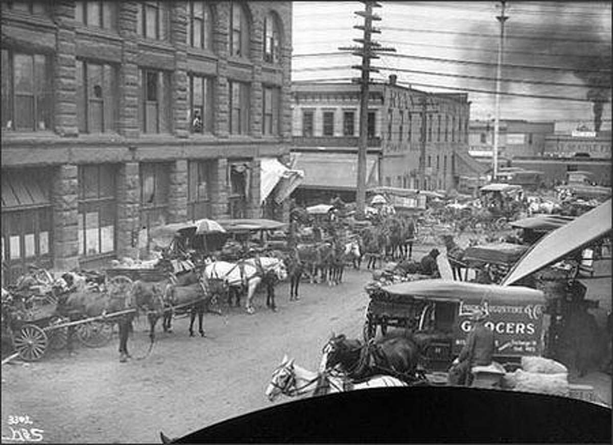 Before the opening of Seattle's Pike Place Market in 1907, farmers sold their fruit and vegetables to the customer through brokers or other middlemen. Much of this wholesale produce trade took place in the so-called Commission District, in the area of Railroad and Western Avenues and Columbia and Marion Streets. Once the wholesalers took their commissions, customers paid more and farmers received only a percentage of the price. Shown are wagons on Marion Street in 1905.