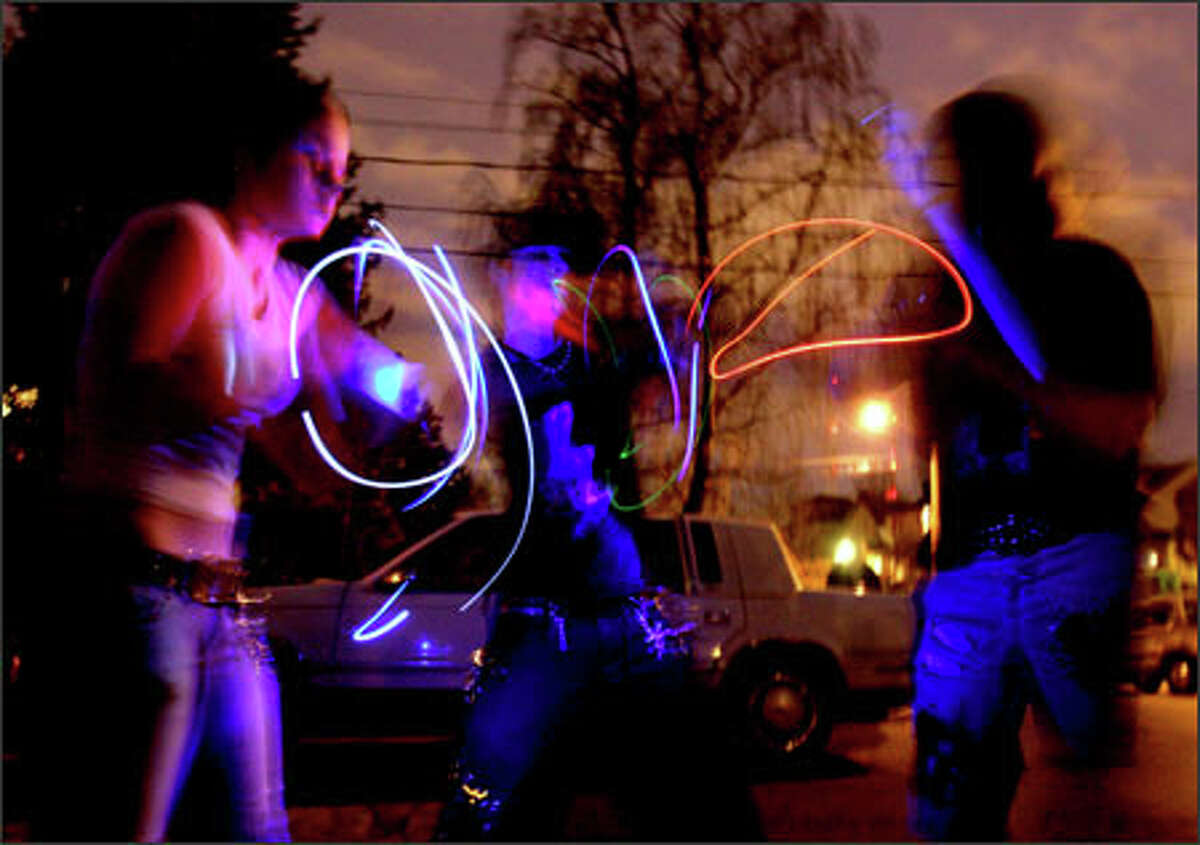 Near the scene of the Capitol Hill shootings, Giggles, 16, left, and Nemesis, 19, center, do a light show on the street as a tribute to "Sushi," their friend who was killed.Schenker: Friends of the ravers that were killed celebrated in the traditional ways: lighting memorial candles, hugs and tears. Then, one night, the not so traditional way to honor one of the murder victims presented itself. This dance with glowing neon tubes was captured using a slow shutter speed.