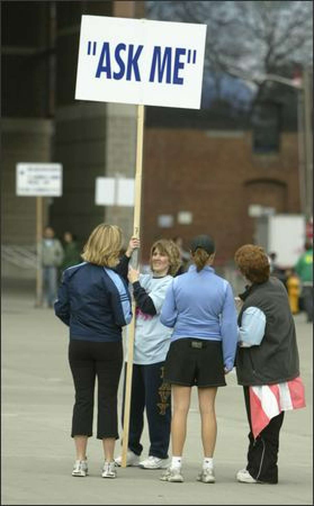 Volunteers Cindy Evans, holding sign, and Kass Klemz, right, give directions to early arriving runners in front of Qwest Field.