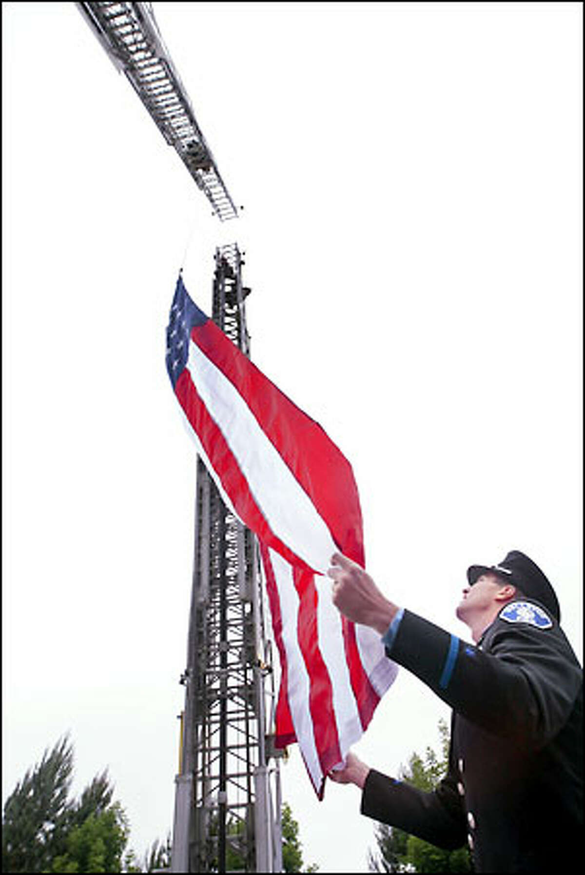 Bellevue firefighter John Harn unfurls a flag as it's raised between the extended ladders of two fire trucks at the scene where Deputy Richard Herzog was slain. A motorcade of hundreds of police cars, ambulances and fire trucks passed under the flag in Herzog's honor.