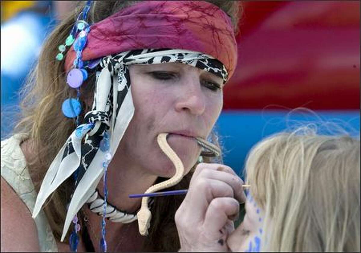 Face painter Jill Sparrow holds a rubber snake between her teeth as she services a customer.