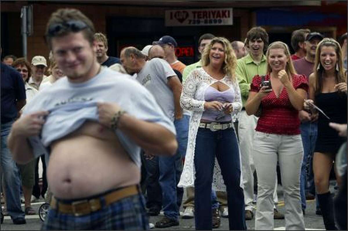 Ryan Carlyle, of Monroe, Wash. shows off his beer belly as Debra Churchill, left, Melissa Olson and Mandy Pemberton, right, of Kirkland cheer during a contest to find the most exceptional belly in the crowd at the Kirkland Classic Car Show.