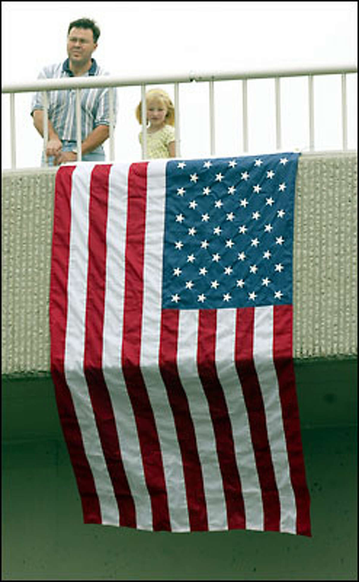 Rob Minor, of Covington, and his daughter Melissa raised a flag on the Covington Way SE overpass near the scene of an accident that killed D.O.T. worker Jake Baardson last week on Highway 18. About 150 vehicles made their way convoy-style from Baardson's memorial service in Kent to the site near Covington.