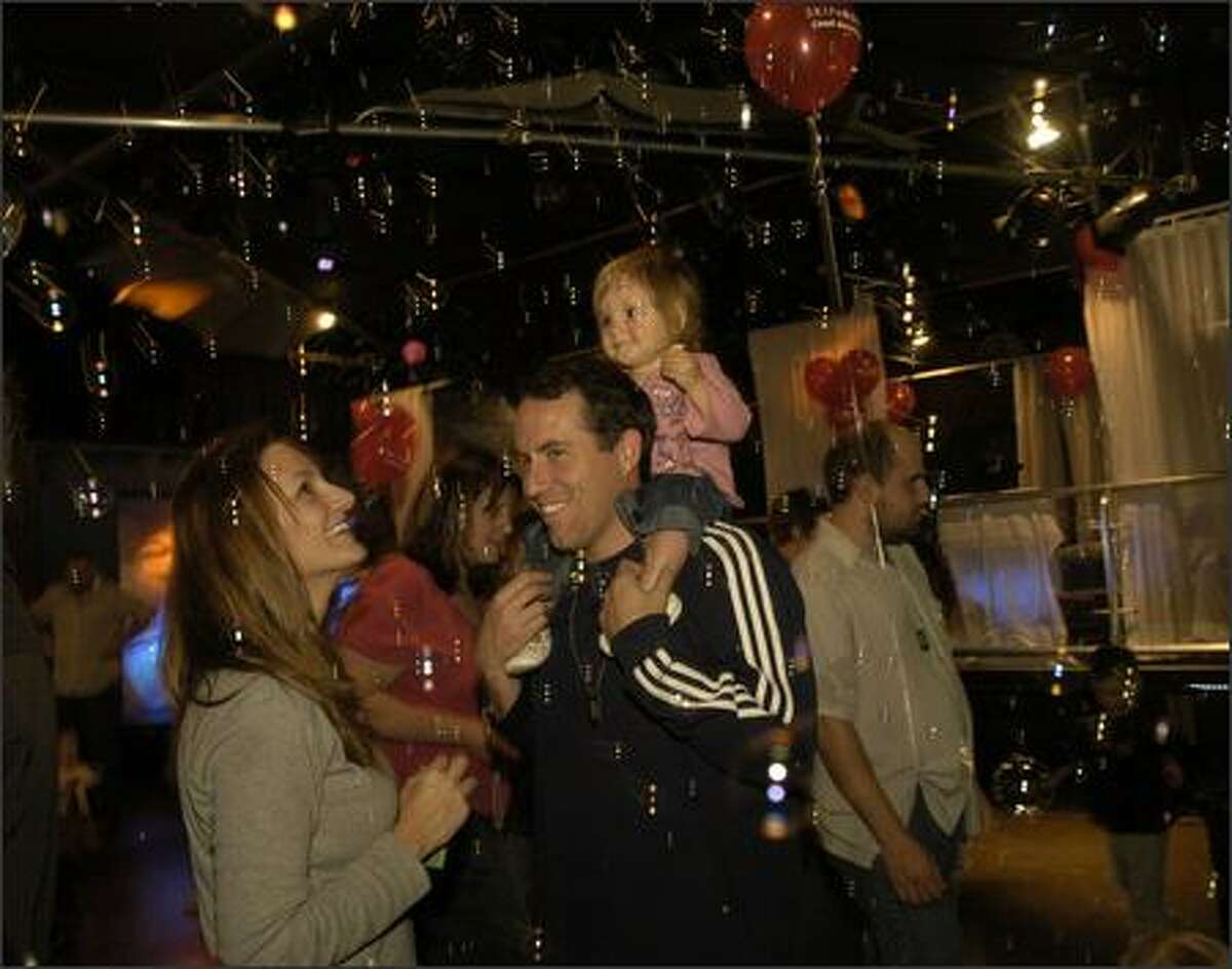 A rain of bubbles falls around Stella Wilson, 15 months, sitting on the shoulders of her dad, Eric, and mom, Ann Hurley.