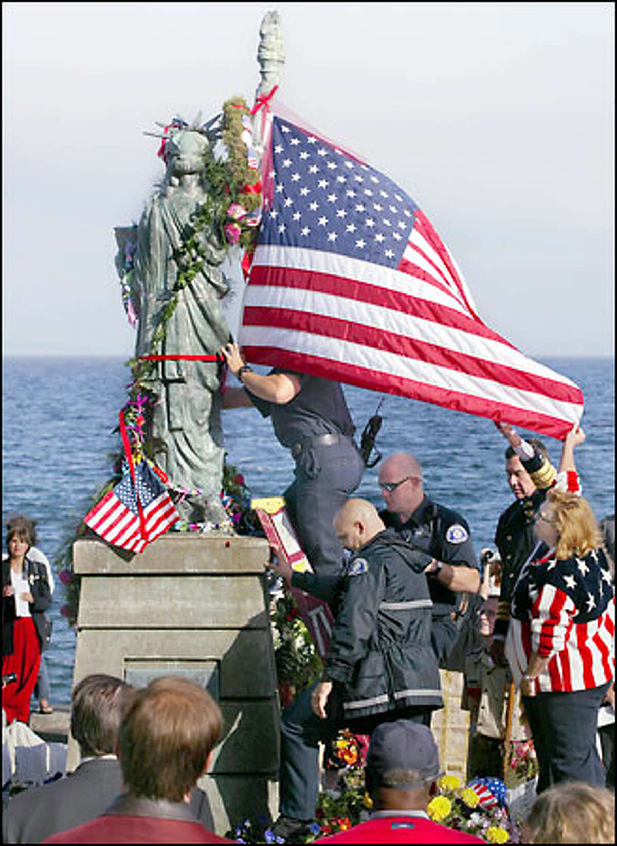 Cindi Laws, bottom right, returned to Alki, where she sought solace last Sept. 11, to place an American flag on the Statue of Liberty. Assisting were Seattle police Chief Gil Kerlikowske, behind her, Seattle firefighters Jason De Bruler, top, Roland Falb, in glasses, and L.T. Grant.