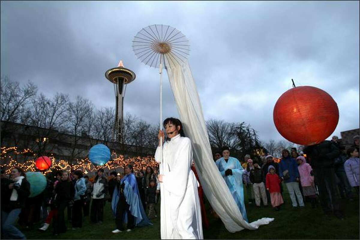 Representing winter, Naho Shioya leads brightly lit lanterns symbolizing planets amid a crowd of onlookers.
