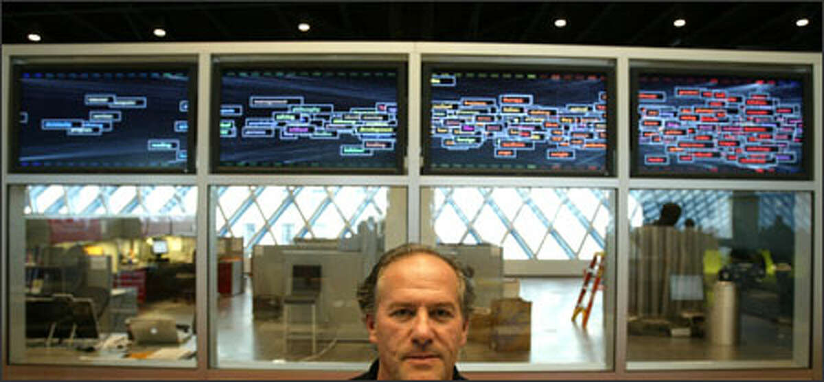 George Legrady poses with his installation, "Making Visible the Invisible," at the Seattle Central Library's Mixing Chamber.