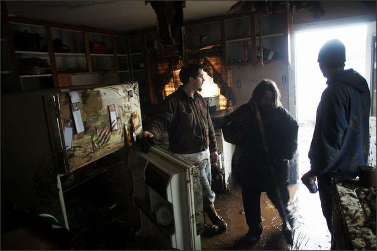 Friend Daryl Reese, left, and home occupants Shandi Perryman and boyfriend Ben Cardin clean massive mud deposits from the floors and walls in Cardin's home near Curtis, Wash.