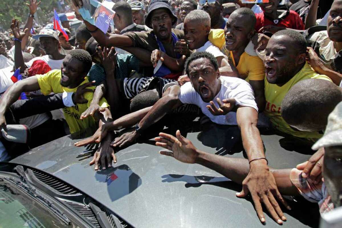 Supporters of Haiti's former President Jean-Bertrand Aristide surround his car as he arrives to his home in Port-au-Prince, Haiti, Friday March 18, 2011. Aristide, who was forced to flee Haiti due to a rebellion in 2004 aboard a U.S. plane, returned after seven years of exile in South Africa, days before Haiti's presidential runoff election Sunday. (AP Photo/Dieu Nalio Chery)