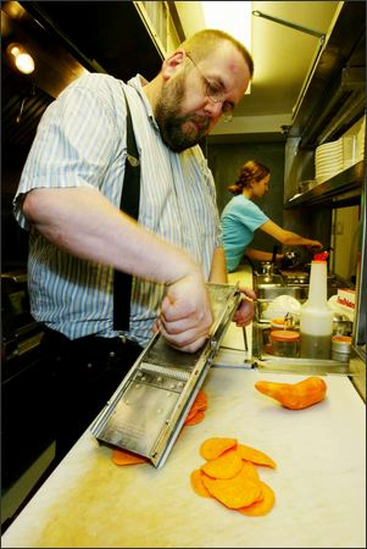Hot Dish co-owner and chef Daniel McGlothlen slices yam chips as Charlotte Elliott, line cook, works in the background.