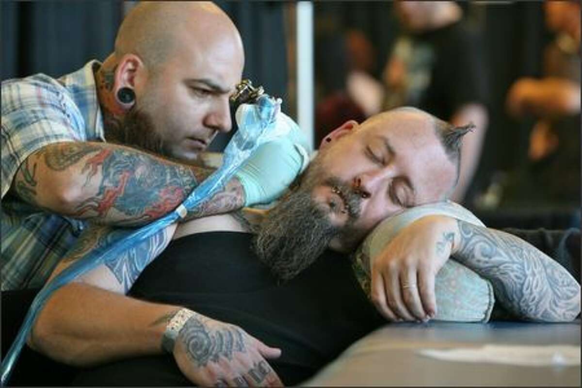 Jason Garza, with Flaming Dragon Tattoo in Tacoma, applies ink to dozing cohort Chris McQueen.