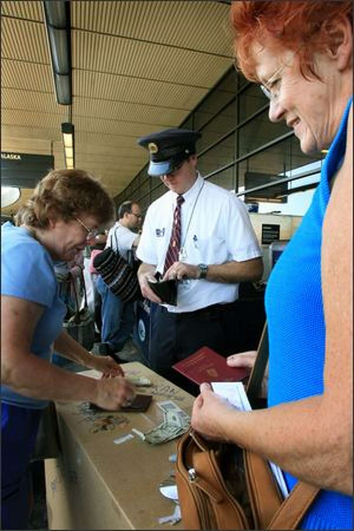 Skycap James Taggart helps Maura Barnes of Seattle, left, and Nuala Gaughran as they search for smaller bills to tip Taggart, who checked in their luggage at Sea-Tac Airport on Friday.