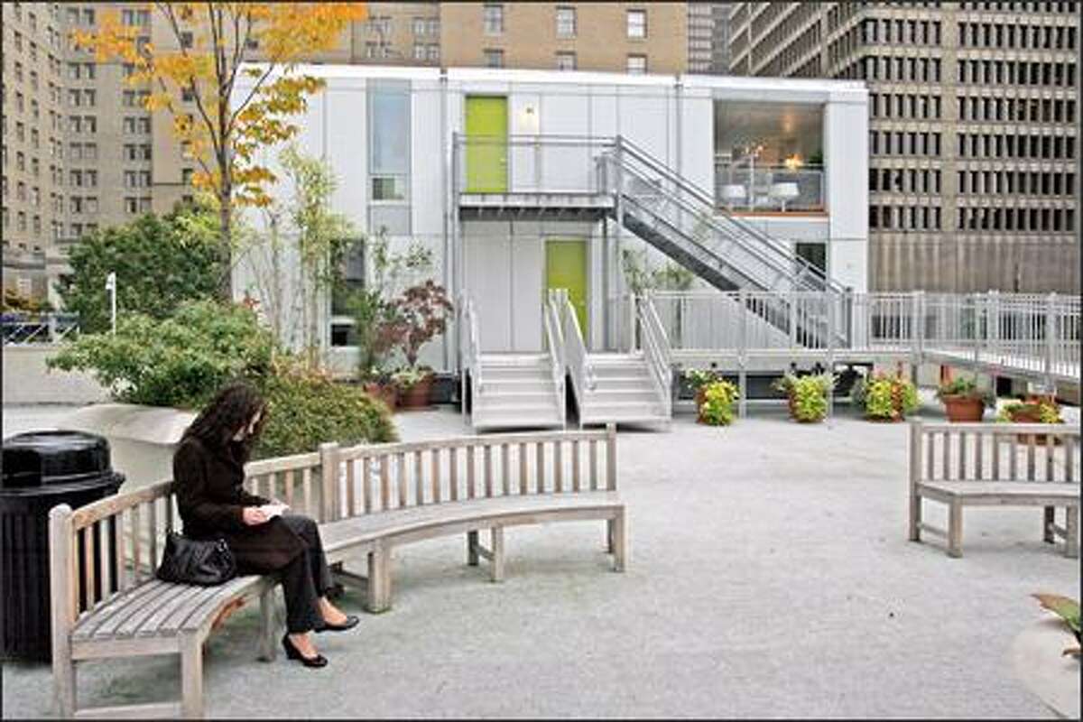 Kristin Osborne of Technology Alliance takes a break Wednesday at the Rainier Square roof park where a pair of Unico stackable modular apartments, in background, are on display.