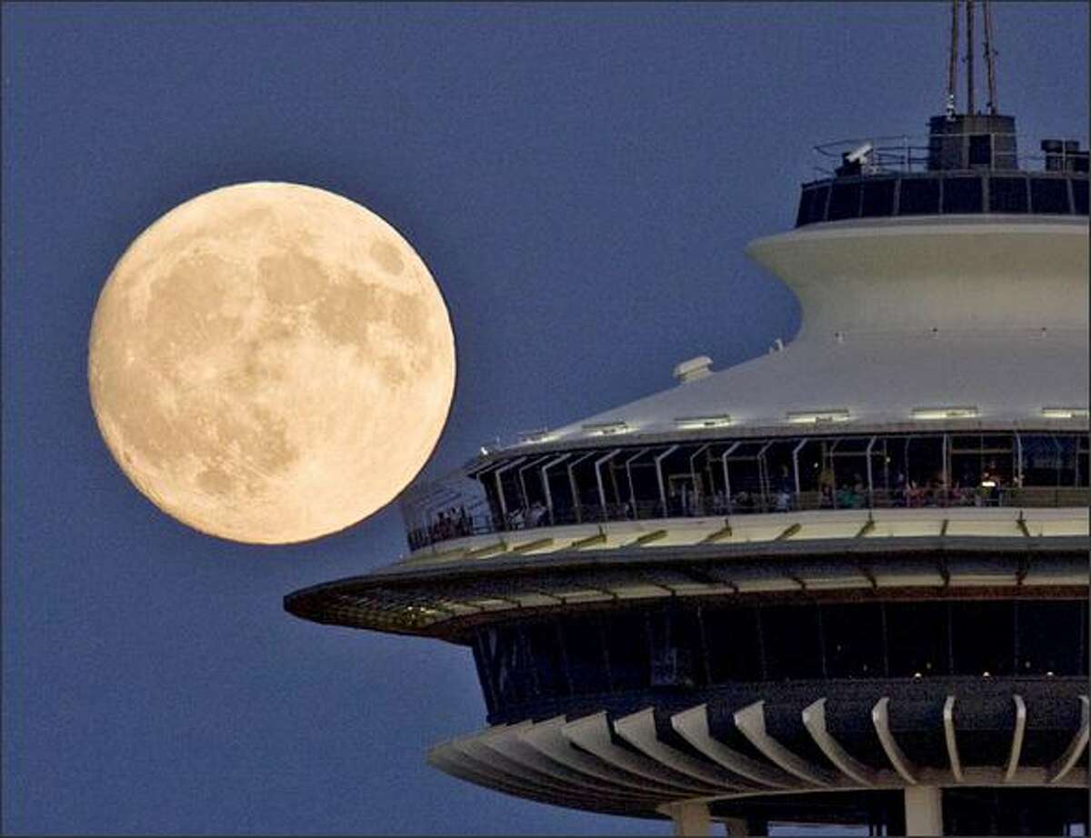 Visitors to the Space Needle enjoy a full moon.Haller: I always find it a challenge to capture a view of the full moon that interests me. Often when I see a full moon start to rise over the Cascade Mountain range, I take off trying to come up with an angle to show something different. Rushing around trying to find something new is a challenge. Once I rushed to Harbor Avenue to make a picture of the moon coming up over downtown buildings, only to have it come up over Beacon Hill. Then rushing around trying to get into a position where a plane taking off from Sea-Tac would pass in front of the moon. The next full moon rise I made a photo of the moon coming up on the left side of a building. A little later that night, I found out that there was another P-I photographer making a photo of the moon coming up on the right side of the building. He was just down the street. Neither one of us knew the other was out shooting the moon.