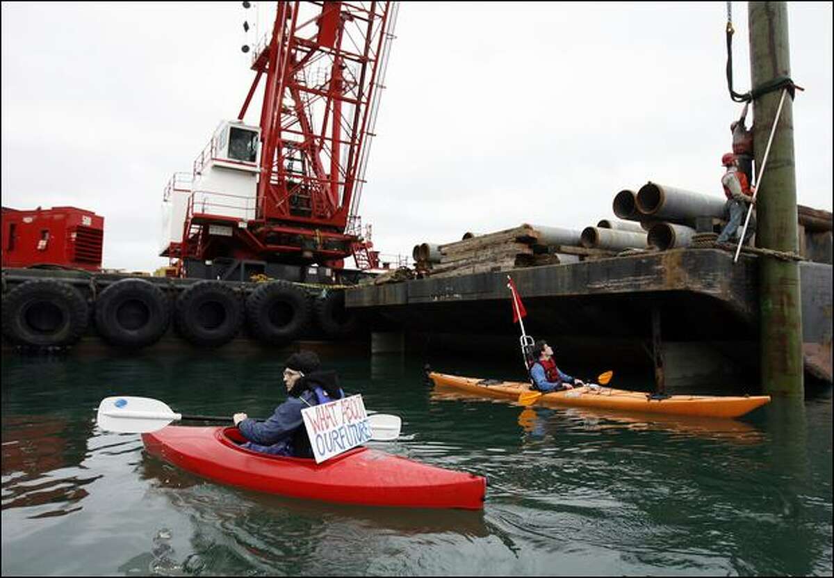 Ignoring a 100-foot restricted zone around the barge, protesters Swaneagle, left, and Logan Price try to disrupt work on a Glacier Northwest gravel mine dock off Maury Island on Tuesday. The dockworkers were securing a 120-foot piling to a construction barge.