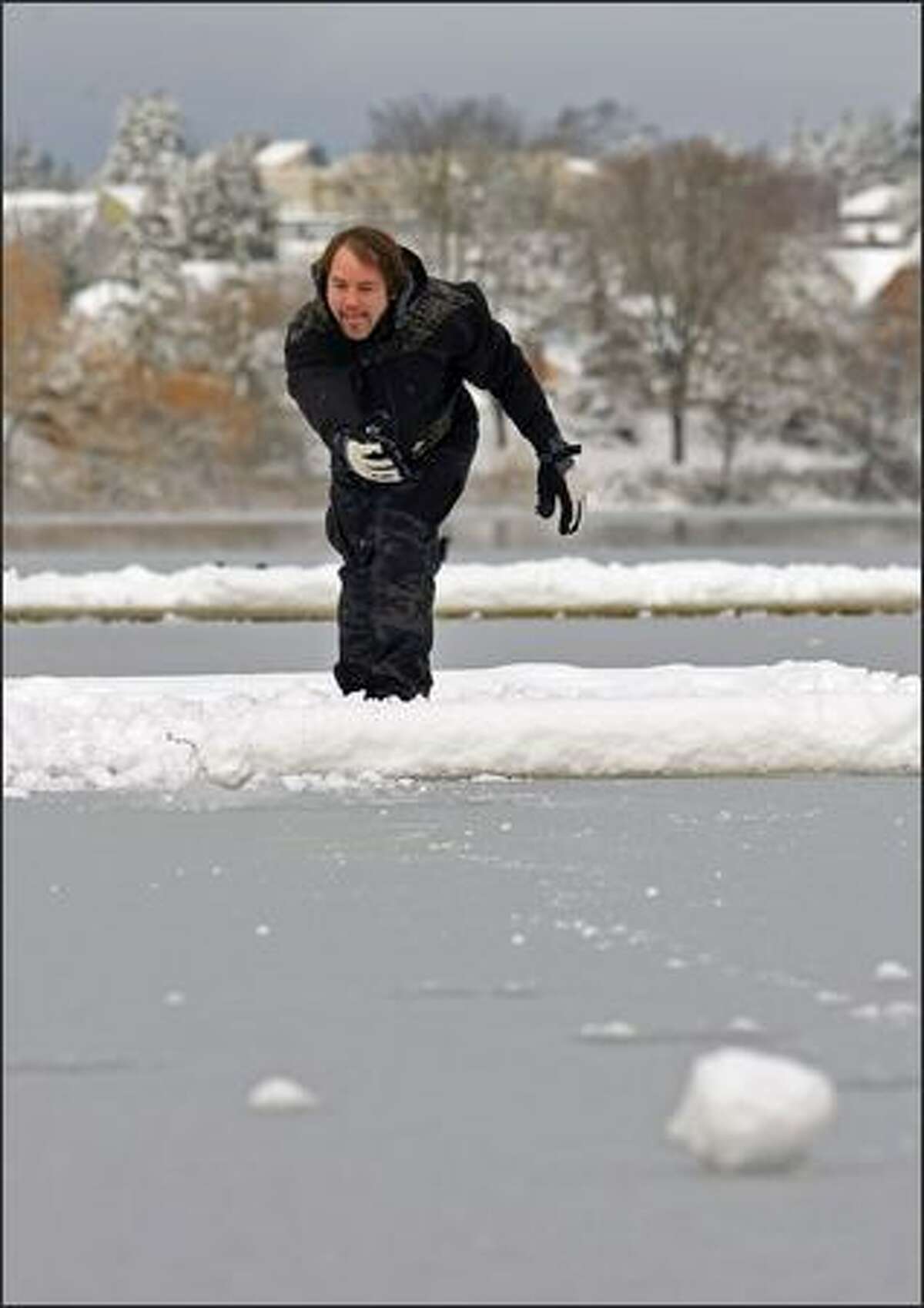 Scott Smith of Seattle lets another snowball roll onto the frozen water while "ice bowling" from the Green Lake docks on Monday.