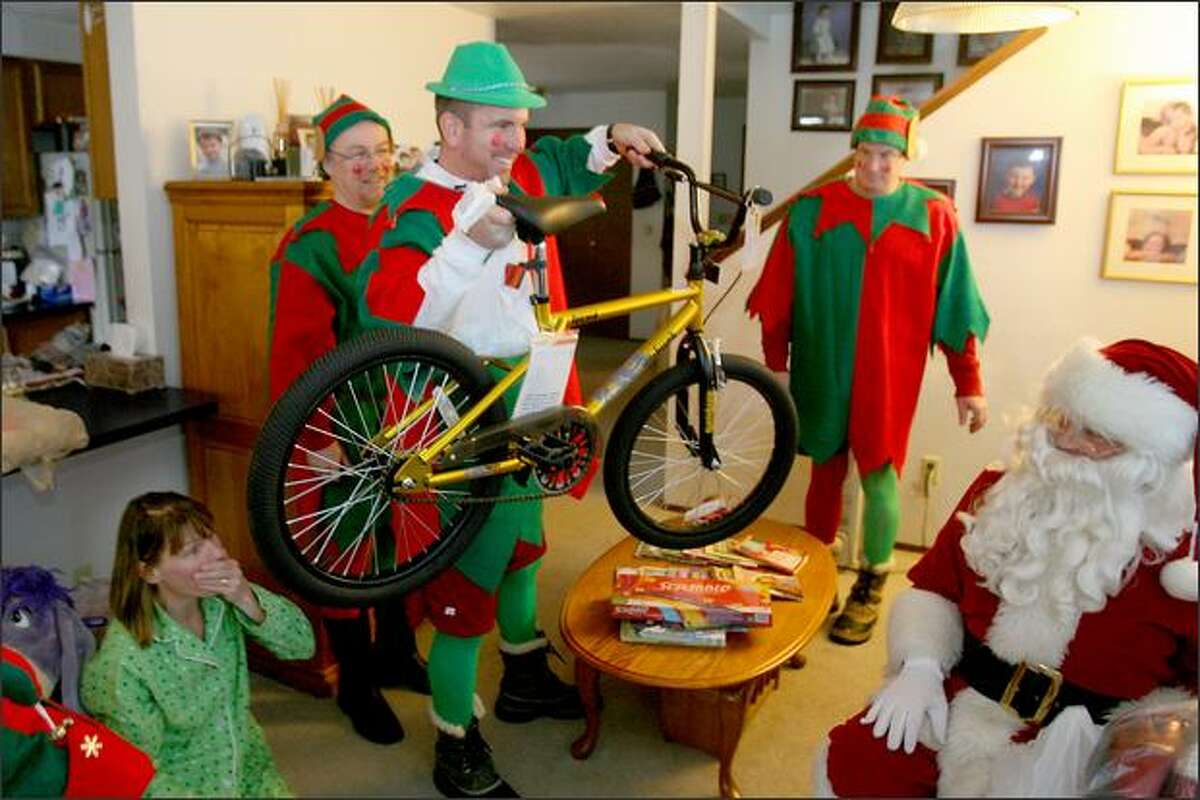 Tami Taylor (lower left) reacts as elf Andrew Walsh with the Forgotten Children's Fund presents a bike to her 10-year-old son Austin (not pictured) at their Seattle apartment.