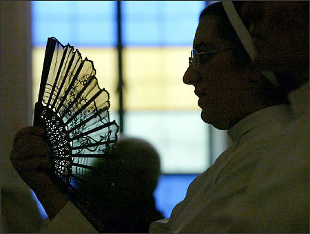 During one of several power outages during mass, Sister Intiqal Ramzi cools herself. Before the war, parishioners said the outages rarely happened during service.
