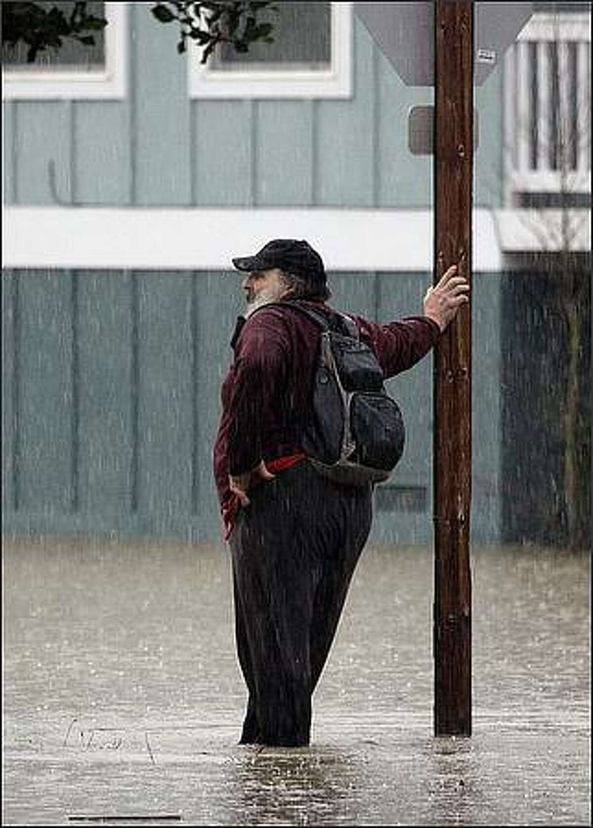 A man takes a break against a traffic sign while wading through floodwater in Snoqualmie, Wash. Rain and high winds lashed Washington state Wednesday, causing widespread avalanches, mudslides, flooding and road closures from rapid snowmelt and the three main highways across the Cascade Range were closed. (AP Photo/Elaine Thompson)