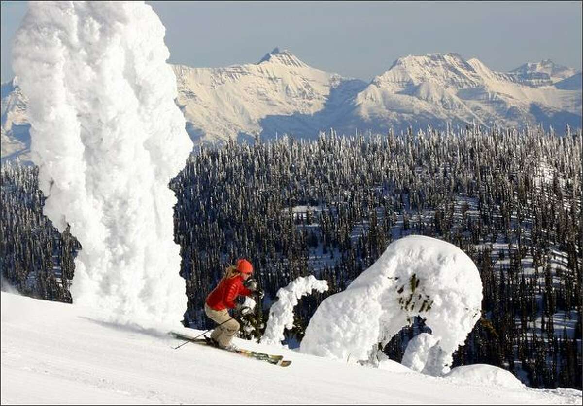 A skier near the summit of Big Mountain at Whitefish Mountain Resort glides by the signature snow ghosts with the peaks of Glacier National Park in the background.