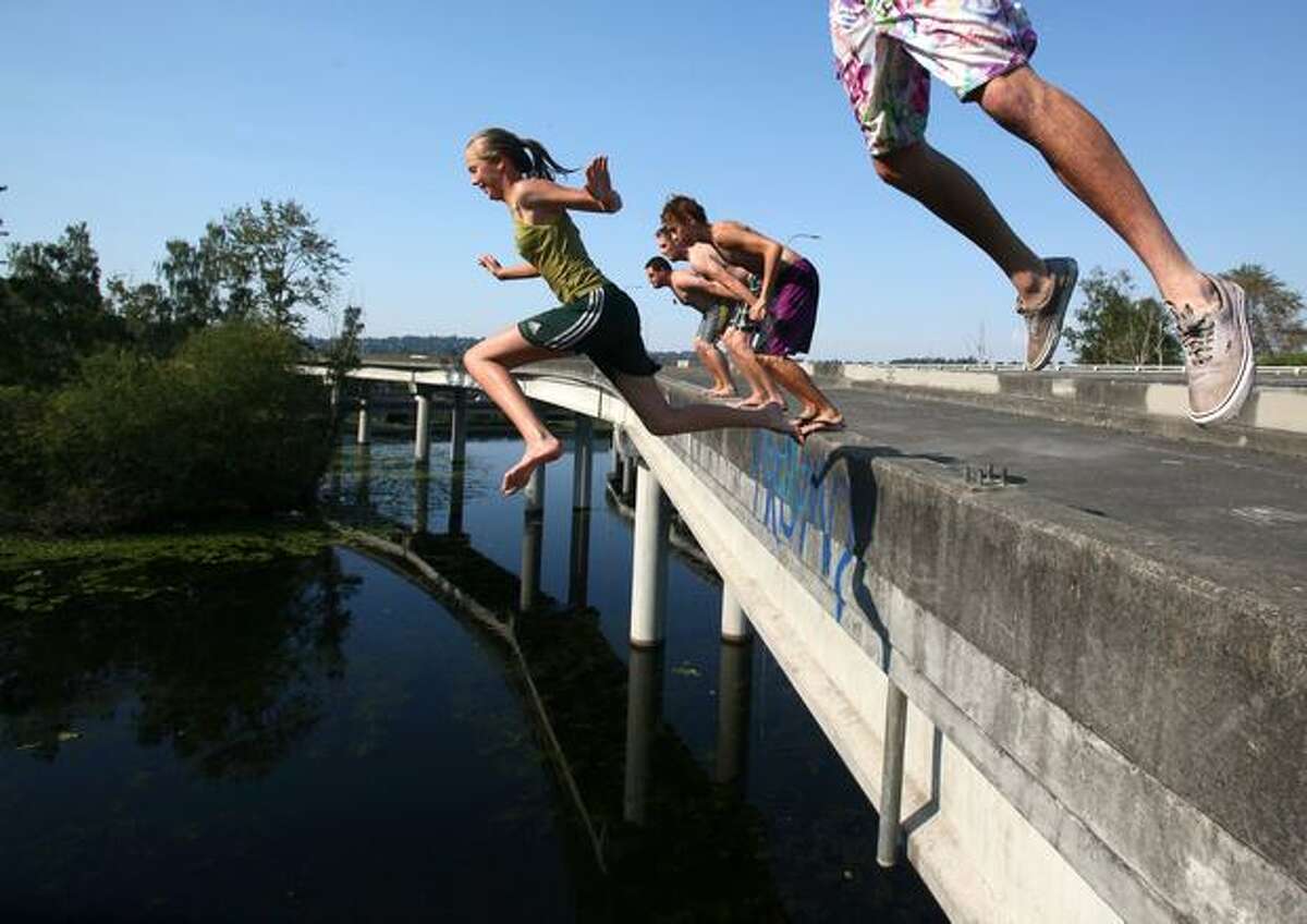Wendy Collins, center, leaps off an unused ramp on Highway 520 into the cool water of the Arboretum below on Tuesday.
