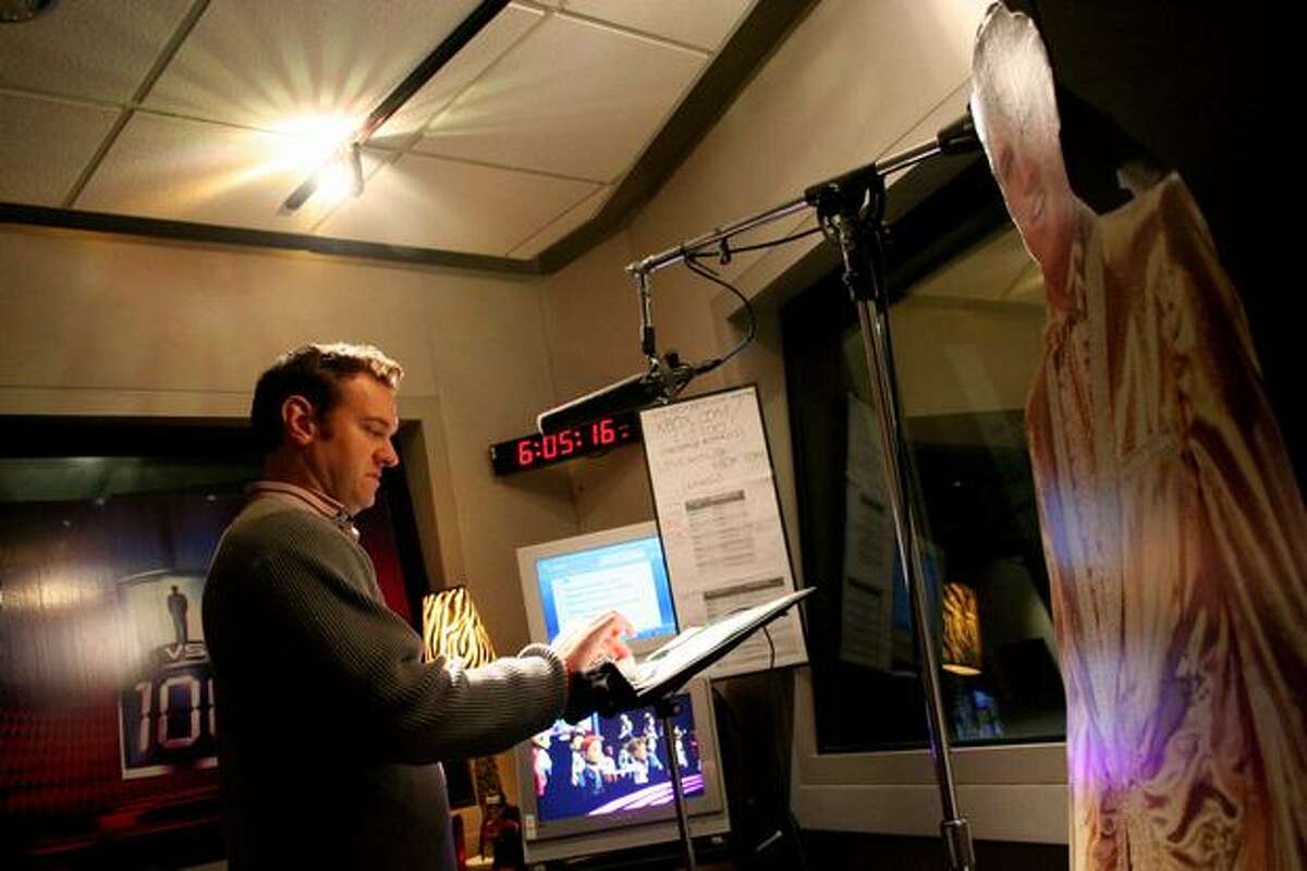 A cardboard cut-out of Elvis watches over host Chris Cashman as he performs in a sound booth Tuesday at Microsoft Studios.
