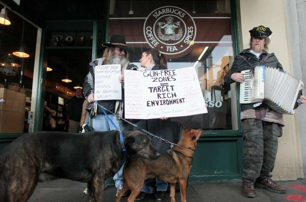 Brick Loomis, left, and Elisa Delaurenti hold signs outside the first Starbucks store, at Seattle's Pike Place Market, opposing a movement to pressure the coffee chain into banning guns from all its stores.