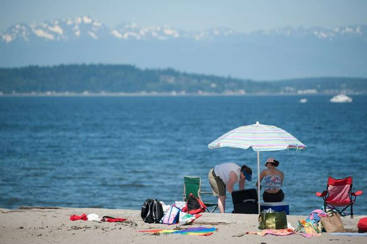 A family sets up an umbrella and lays out towels at Alki Beach on a day when temperatures broke the 90-degree mark.