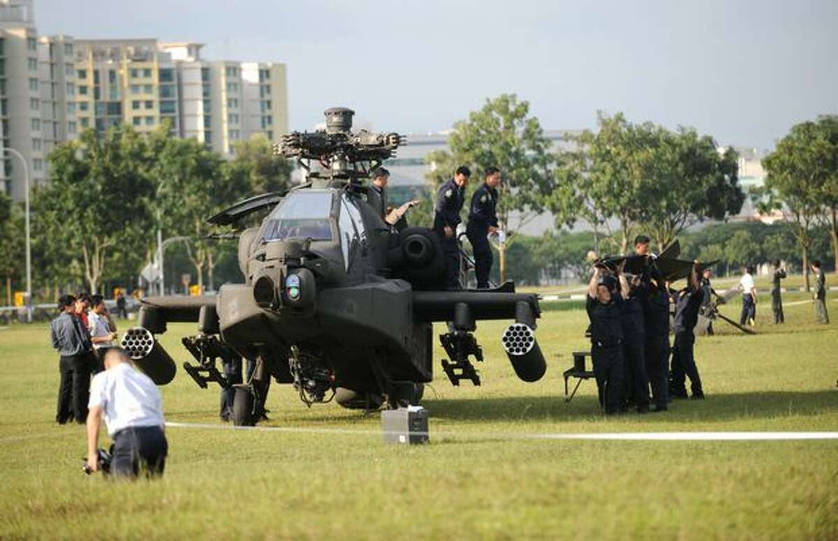 A Republic of Singapore Air Force Apache AH-64 helicopter sits on a field as its tail is carried by air force engineers after it crashed in Singapore.
